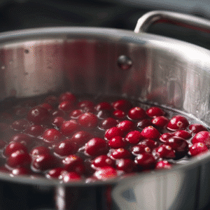 Cranberries gently boiling in a stainless steel pot on the stove
